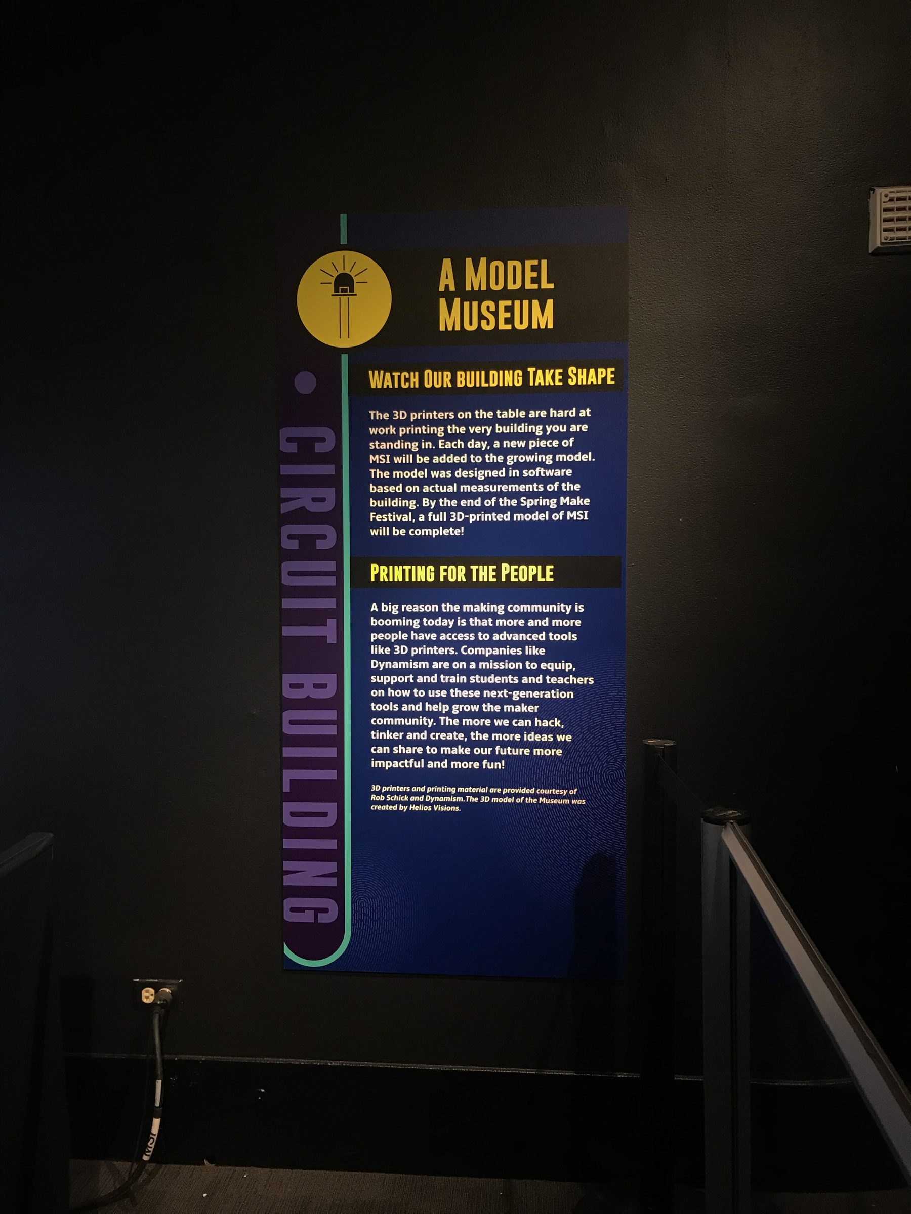 Tall blue exhibit sign titled A Model Museum with sections headed Watch Our Building Take Shape and Printing for the People.