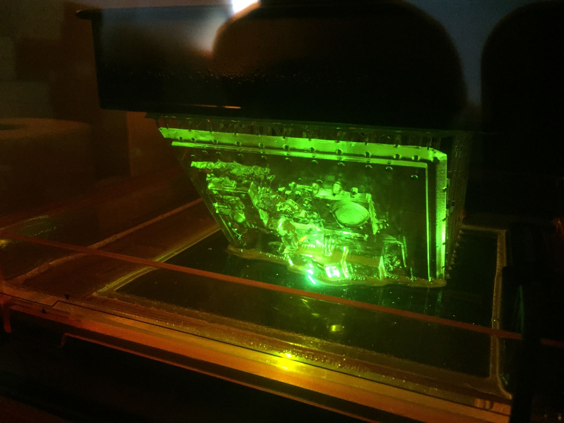 Inside a Formlabs Form 2 resin printer, a small model of the museum hangs from the build plate, lit green through the orange cover.