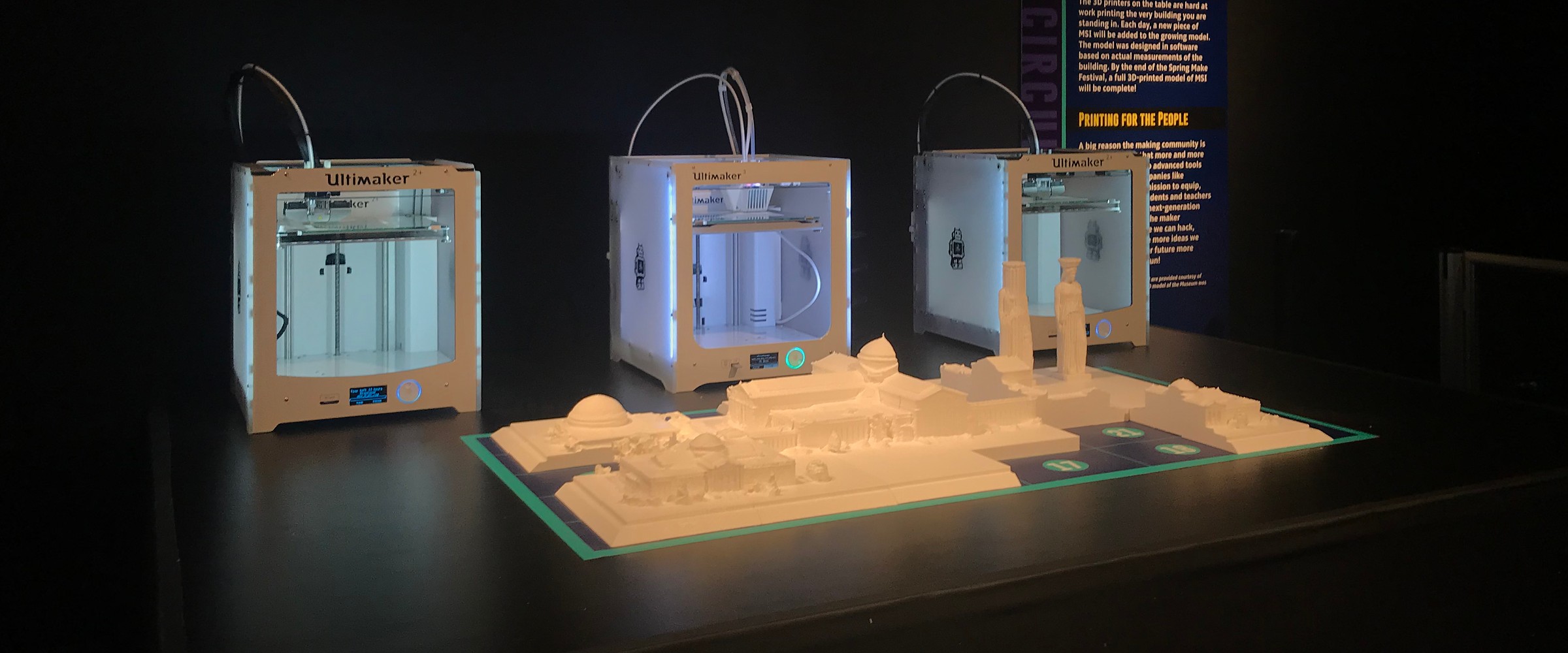 Straight-on view of the white 3D-printed MSI building model on its numbered tile mat, with three Ultimaker printers lined up behind it at the Museum of Science and Industry, March 2018.