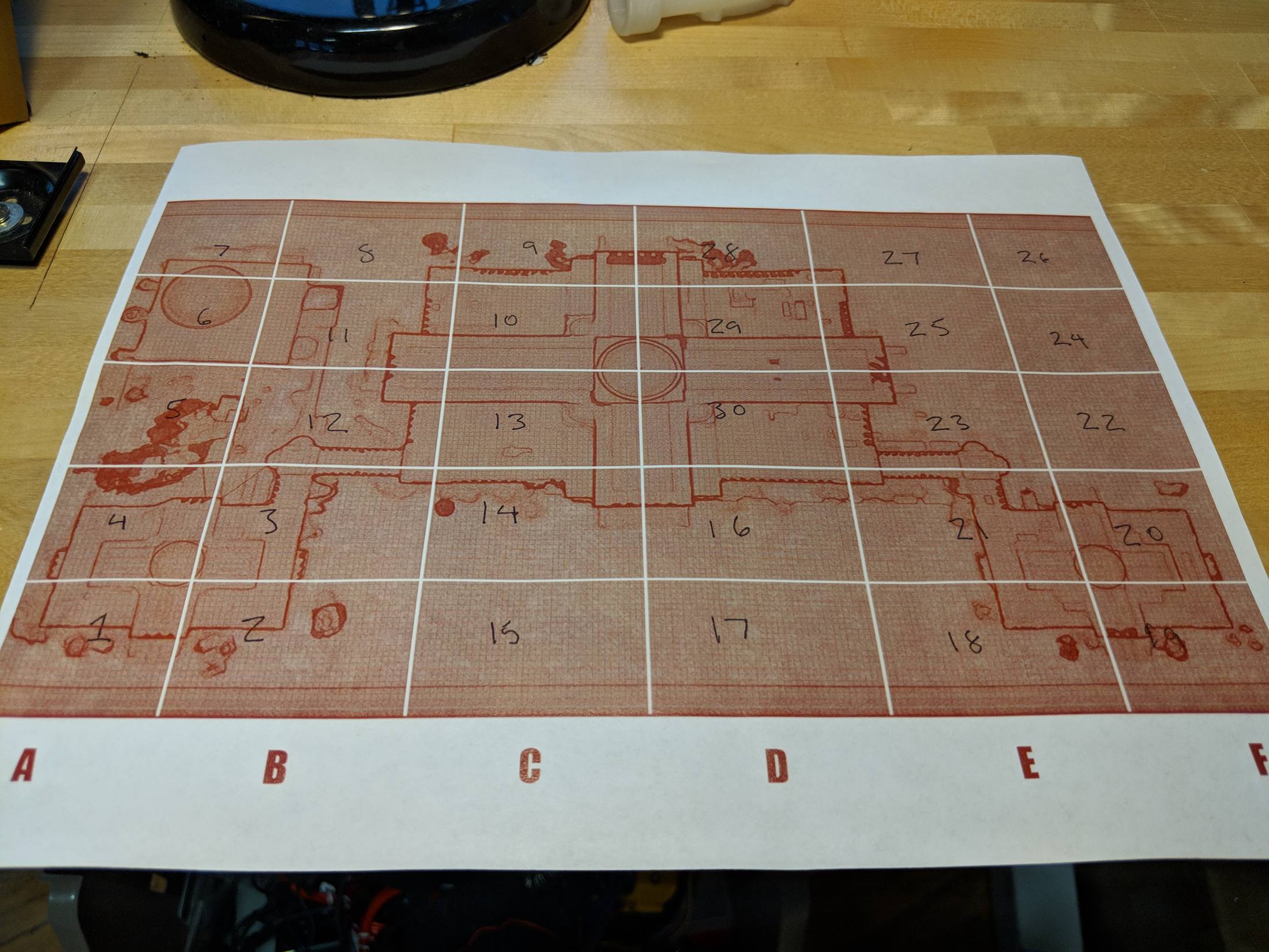 A large sheet of paper on a table printed with the red outline of the museum and a lettered grid.
